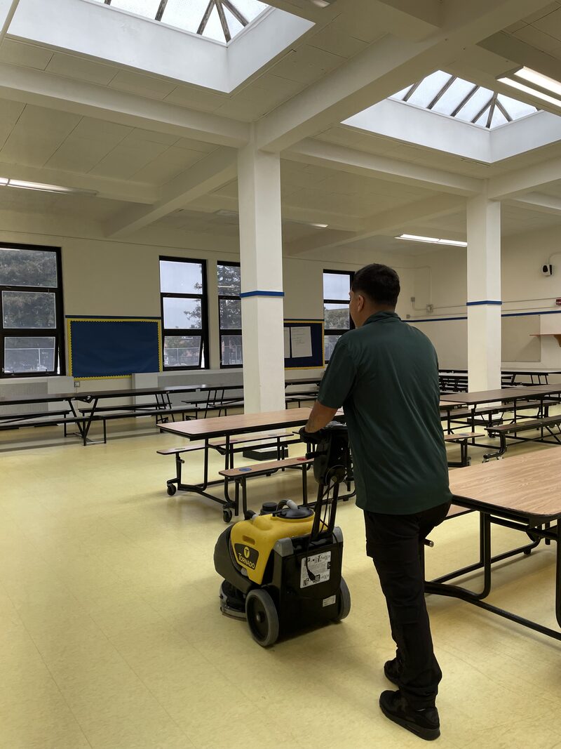 Star's Janitorial Services team member running a walk-behind floor scrubber in a school cafeteria