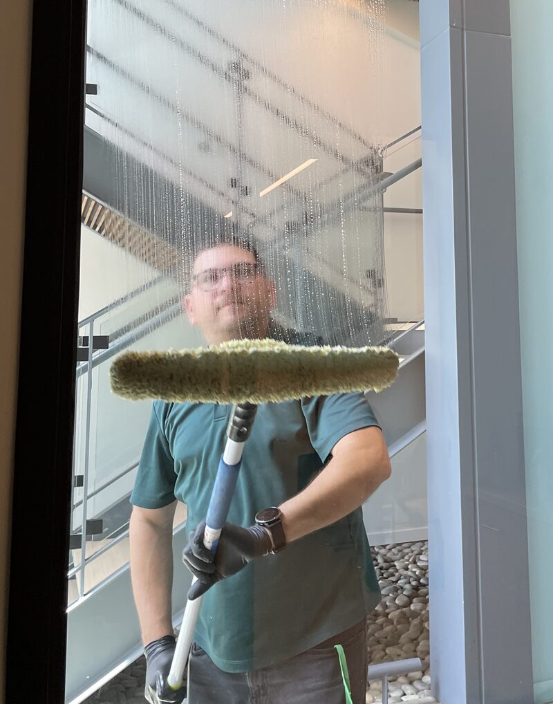 Star's Janitorial Services team member washing an interior glass panel, photographed through the wet glass